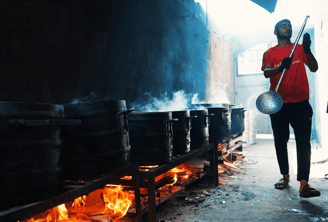 Man stirring large pots over open flames, preparing food for relief efforts in Palestine. Crypto donations like Tether support this vital aid.