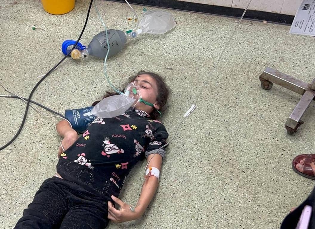 Child with oxygen mask on floor in crisis, needs food, water, shelter, medical care. Donate crypto like SOL to Aid Palestine.