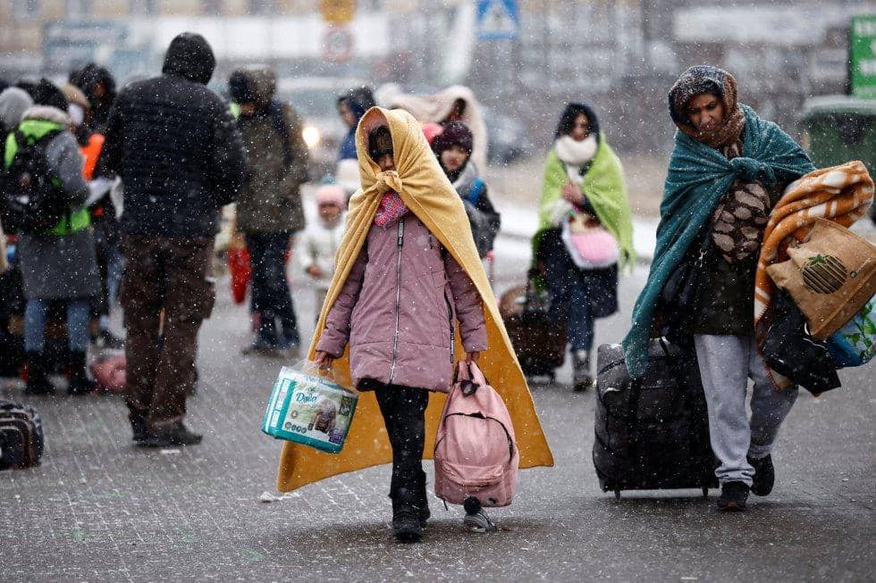 A group of people, including children, carrying bags and blankets, walk through falling snow, symbolizing displaced Ukrainians receiving aid via BTC donations for essentials like water and medical supplies.