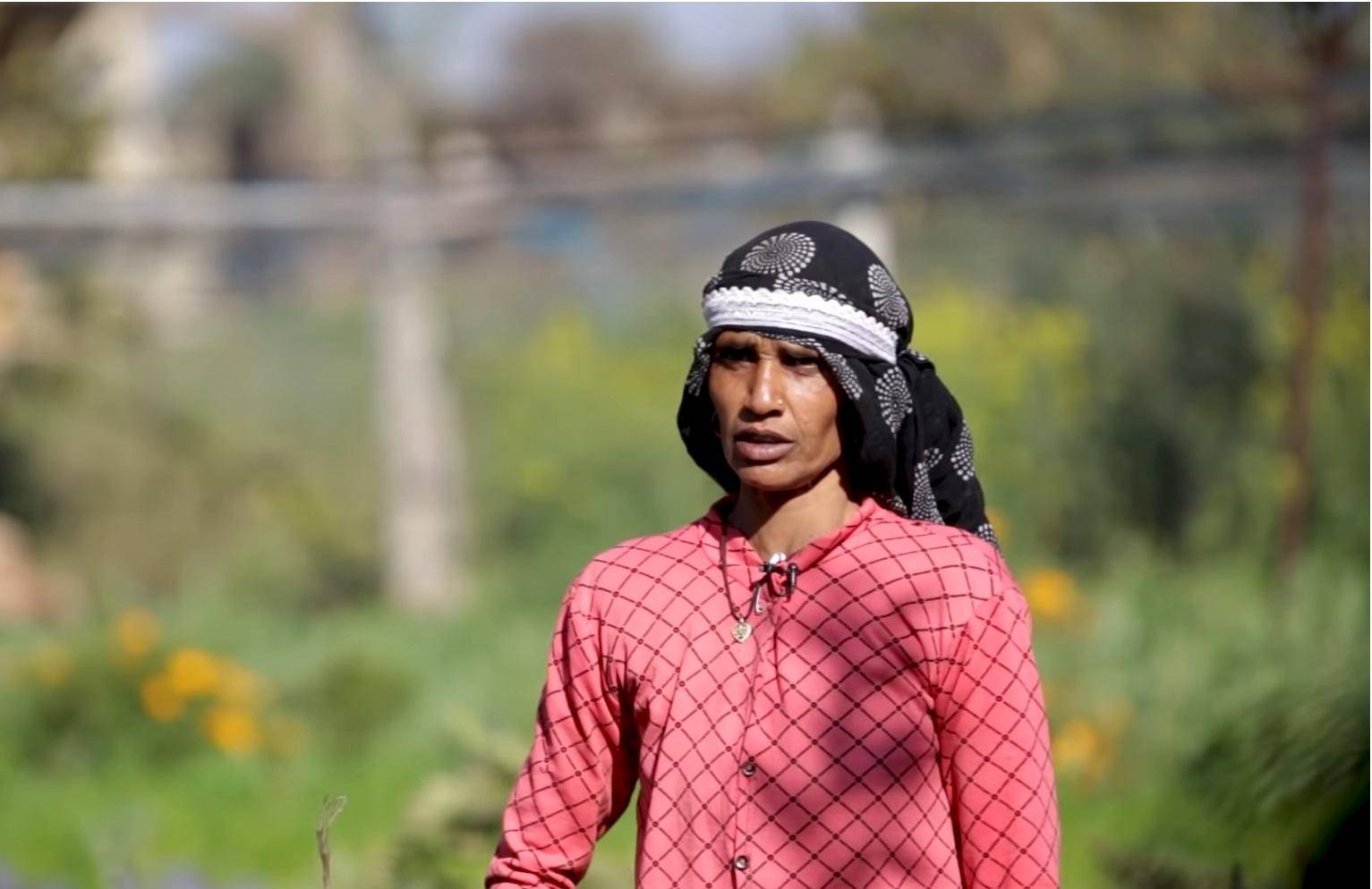Woman in a pink checkered shirt and headscarf in a field, representing crypto donations empowering families through hydroponics and sustainable agriculture.