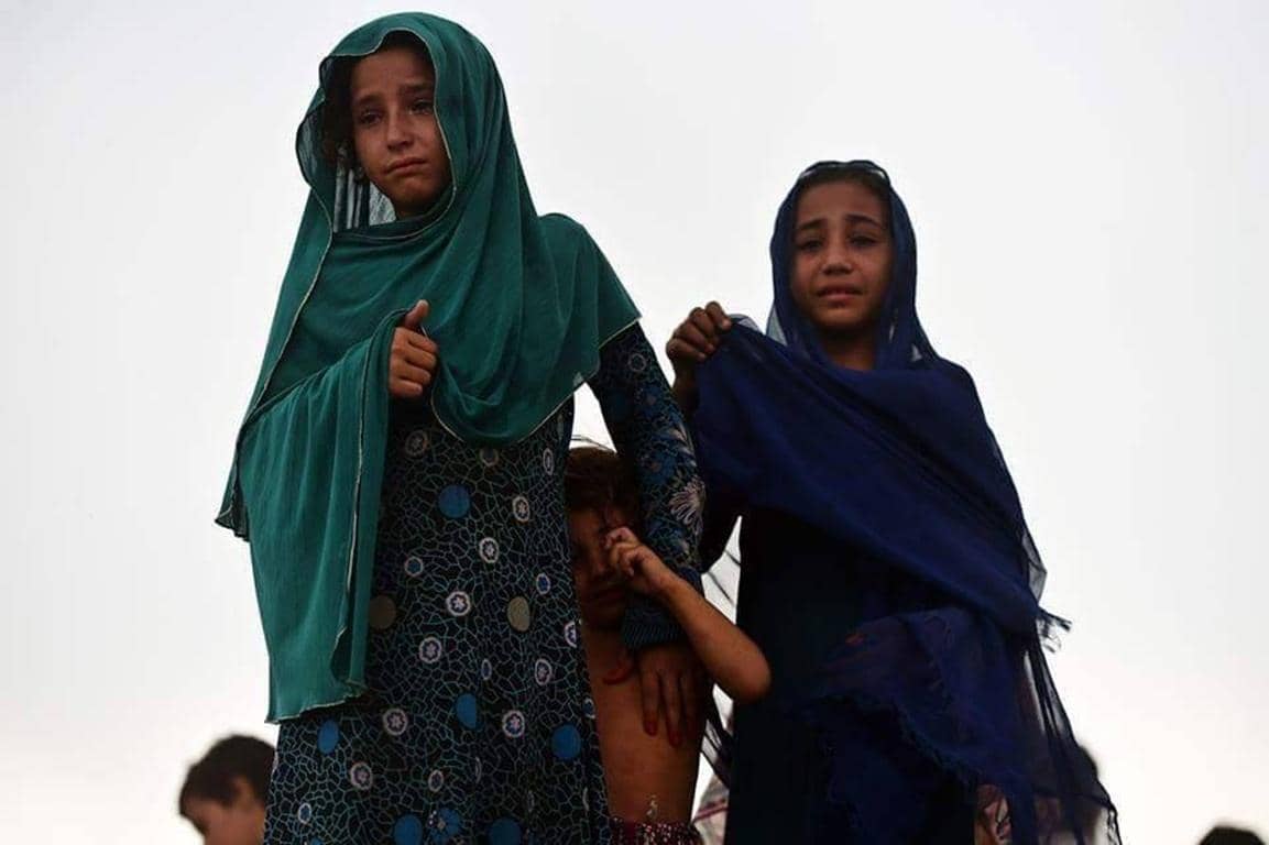 The image depicts two young girls, appearing distressed, one of whom holds another child. Their expressions convey sadness and hardship, linking to the concept of Kaffarah payments for Ramadan breaking fast, possibly with Bitcoin, supporting needy children in crisis regions.
