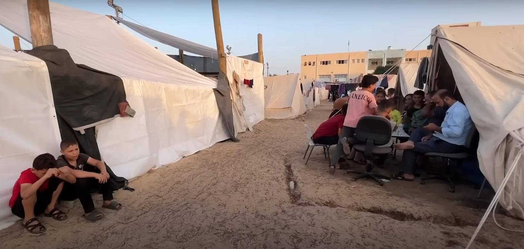 Children in a Palestinian refugee camp gather near tents, some sitting and looking concerned. Others interact with adults, highlighting the daily struggles and need for aid, supported by Ripple (XRP) donations.