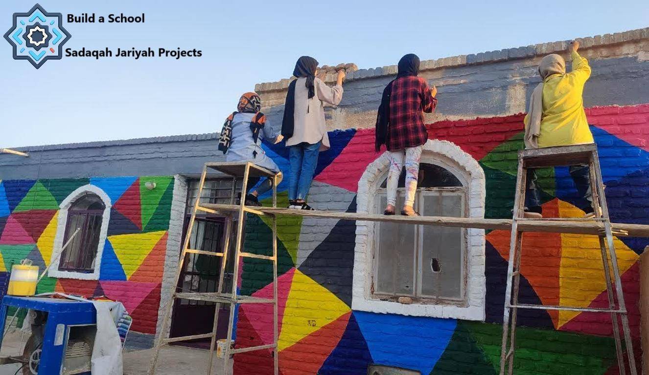 Building a school wall with colorful geometric patterns by four people painting, representing Sadaqah Jariyah projects and ongoing charity, funded by crypto donations like Stellar.