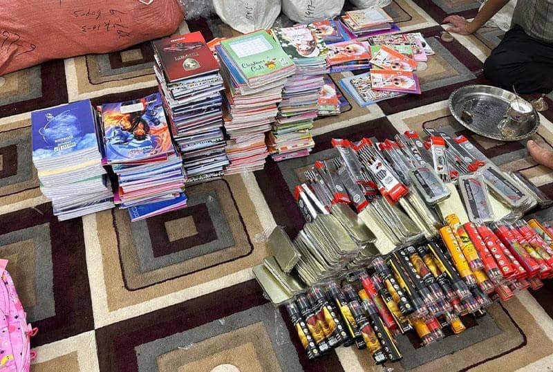 Stacks of school notebooks and writing supplies, including pens and pencils, arranged on a carpet, representing crypto-funded educational aid for disadvantaged children, supported by XRP.