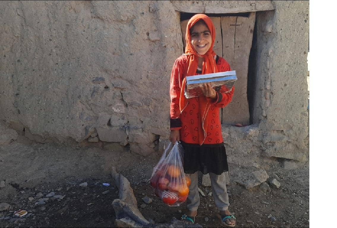Smiling girl in headscarf holding books and a bag of fruit, supported by BTC crypto donations for a stronger Muslim community. Celebrating Prophet's birthday with generosity.