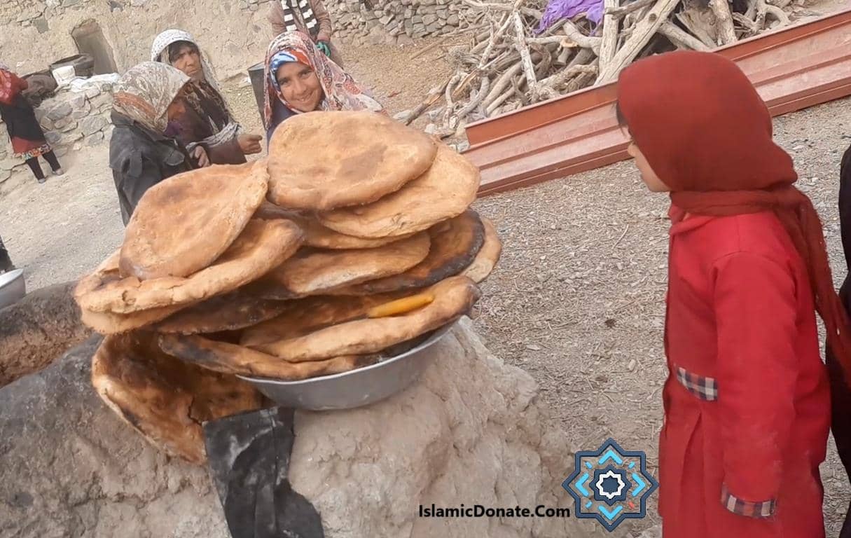 Women and children gather around a large pile of fresh flatbread, signifying a communal charitable act of giving during Mawlid, supported by crypto donations via BTC.