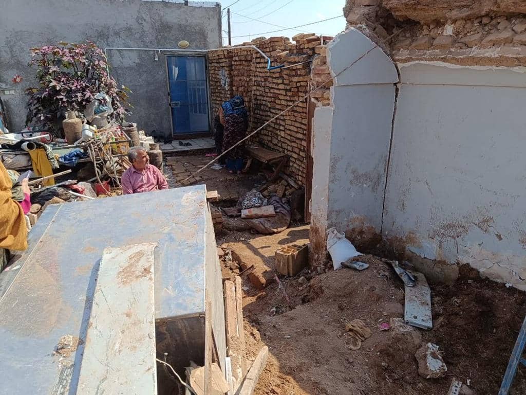 A man sits amidst rubble next to a damaged structure, representing the urgent need for winter aid. Your crypto donation, perhaps in BTC, provides warm clothing, shelter, and heating for vulnerable families in conflict zones.