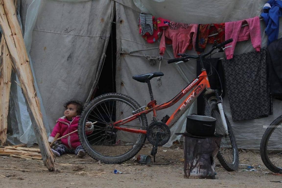 A young child sits by a makeshift tent, with a bicycle and drying clothes nearby, symbolizing the need for aid supported by ETH donations for impoverished families.