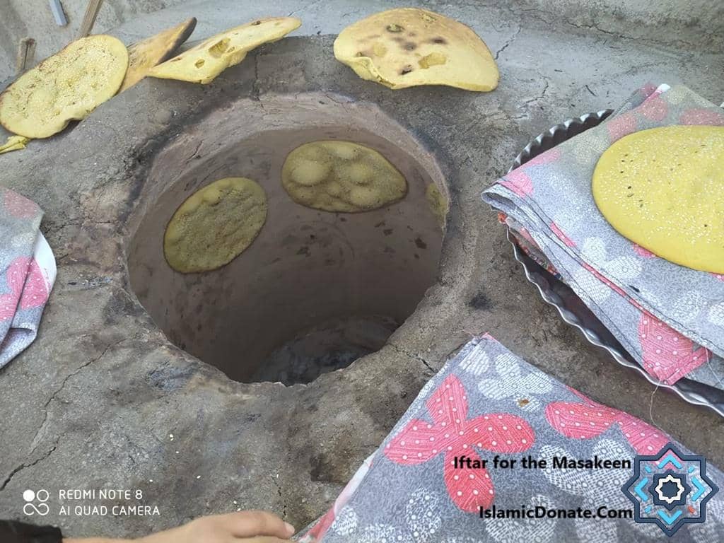 Flatbreads baking in a traditional clay oven, with stacks of freshly baked bread on a patterned cloth, symbolizing iftar for the needy, supporting crypto zakat donations via ETH.