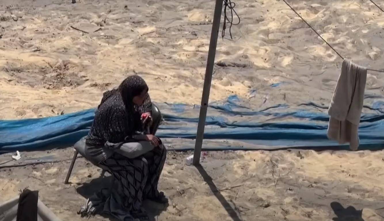 Palestinian woman sits under a tarp, symbolizing the need for humanitarian aid. Crypto zakat donations via USDT can help provide food, water, and medicine.