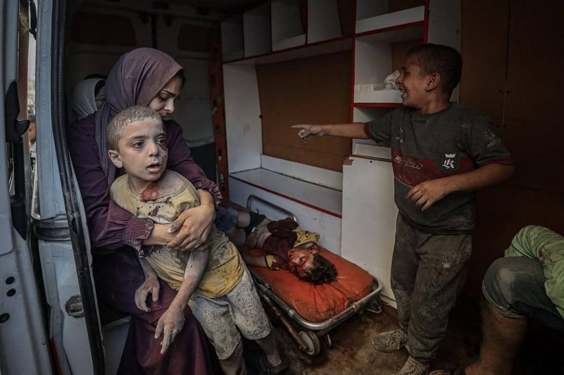 A woman in a hijab holds a bloodied child in an ambulance while another child points, highlighting the urgent need for humanitarian aid and Zakat donations to Palestine. Donate crypto like PYUSD or RLUSD for relief.
