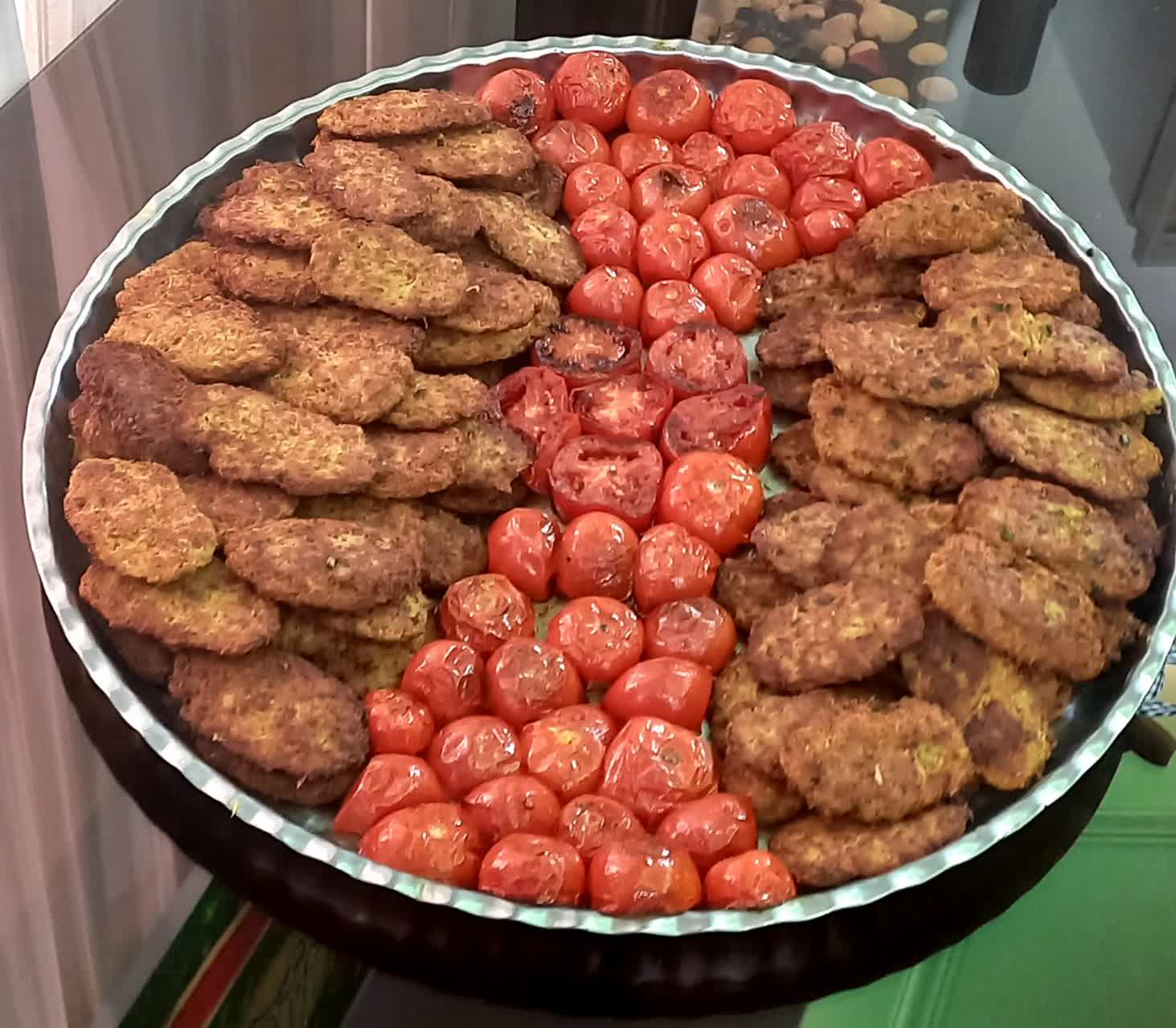A large platter of food featuring patties and roasted tomatoes, representing Iftar meals distributed by Our Islamic Charity, supported by crypto donations like BTC.