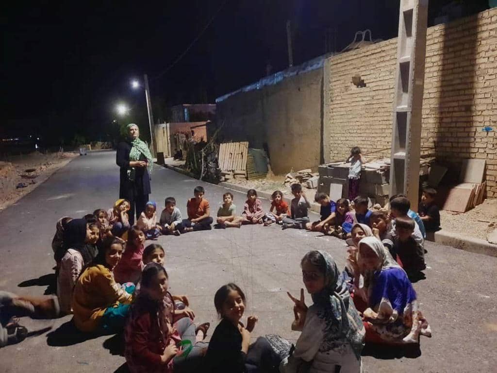 Group of Palestinian children sitting in a circle on a street at night, listening to an adult. They are receiving aid, possibly funded by crypto donations like BCH.