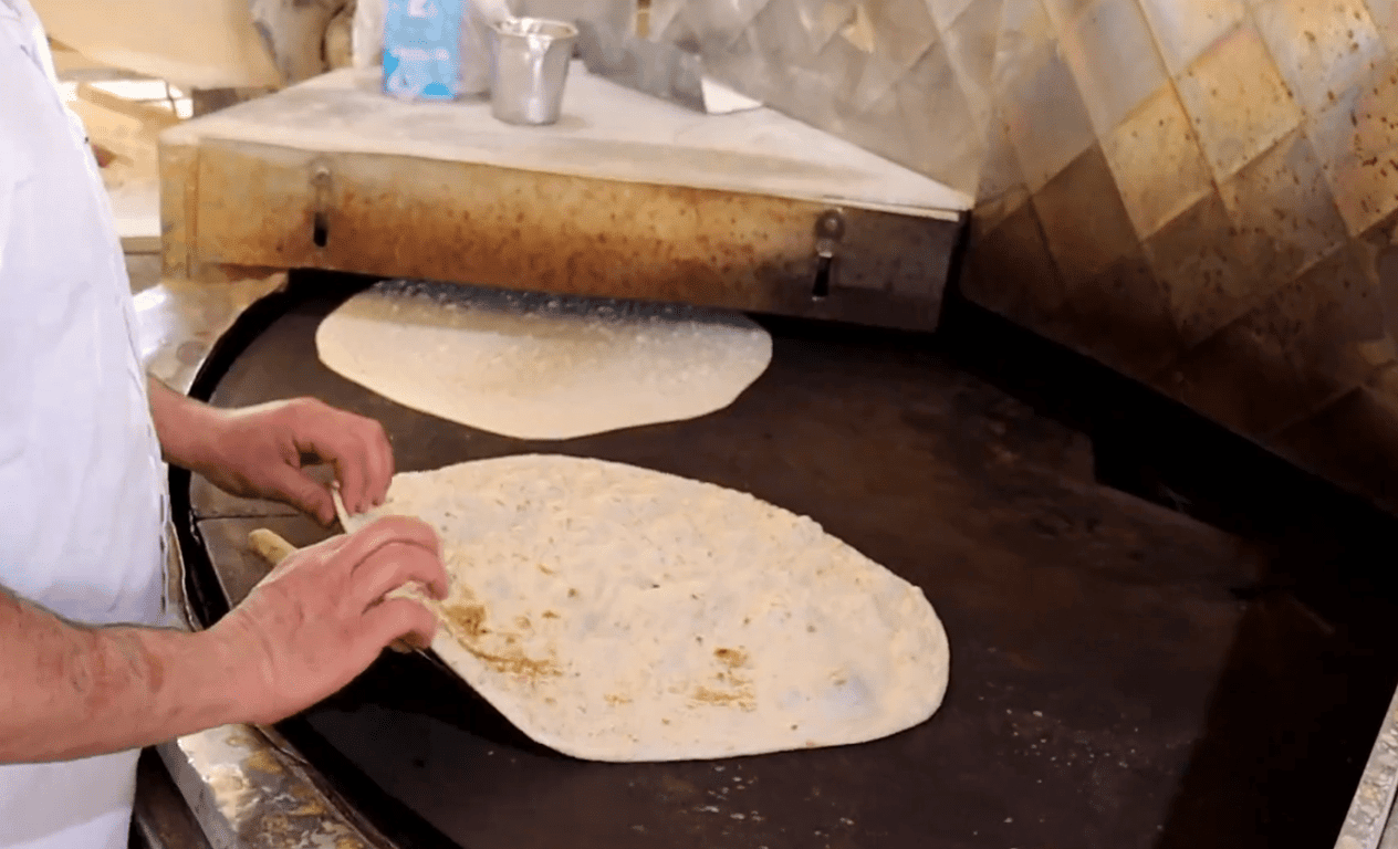 Baker preparing flatbread on a large circular grill, distribution of bread as aid in Gaza, with funds potentially transferred via Bitcoin.
