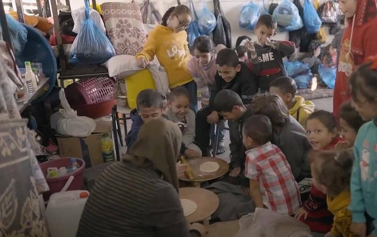Children gather around as a woman prepares dough for bread, a scene of hope delivered by humanitarian aid supported by ETH donations.