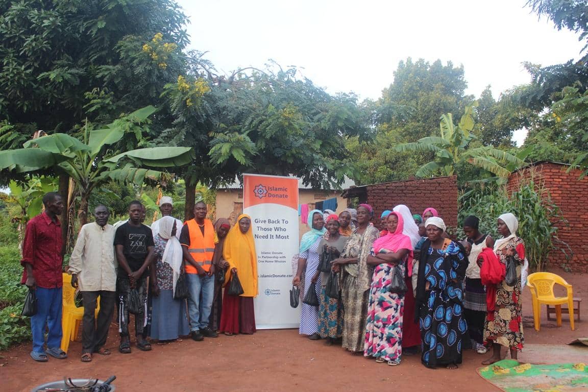 A group of people, both men and women, stand together in front of a banner for Islamic Donate, which reads "Give Back To Those Who Need It Most." The scene depicts community support and aid efforts, possibly supported by crypto donations like XRP.