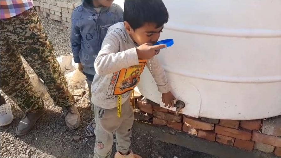 Child drinks water from a tap on a large white tank, crypto-supported aid bringing clean water to needy families.