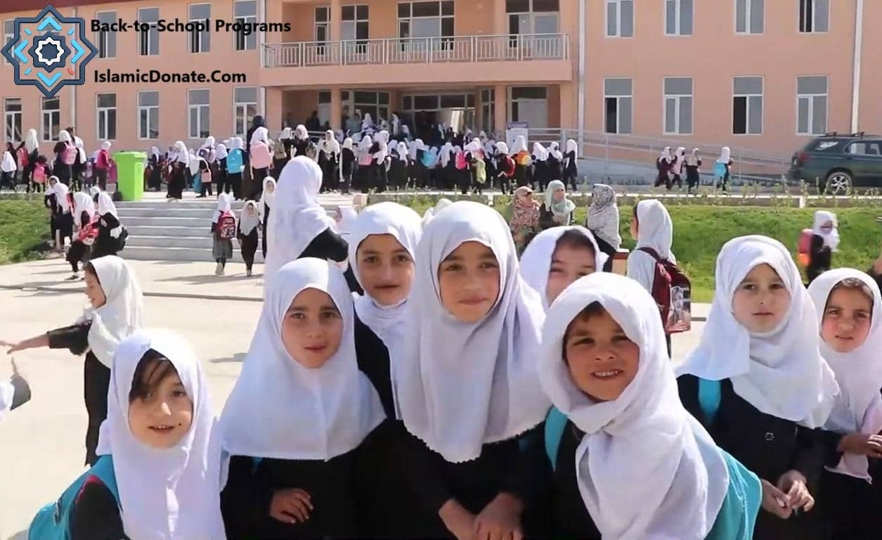 Group of young girls in hijabs smiling in front of a school building, part of Sadaqah Jariyah education projects supported by BTC donations.