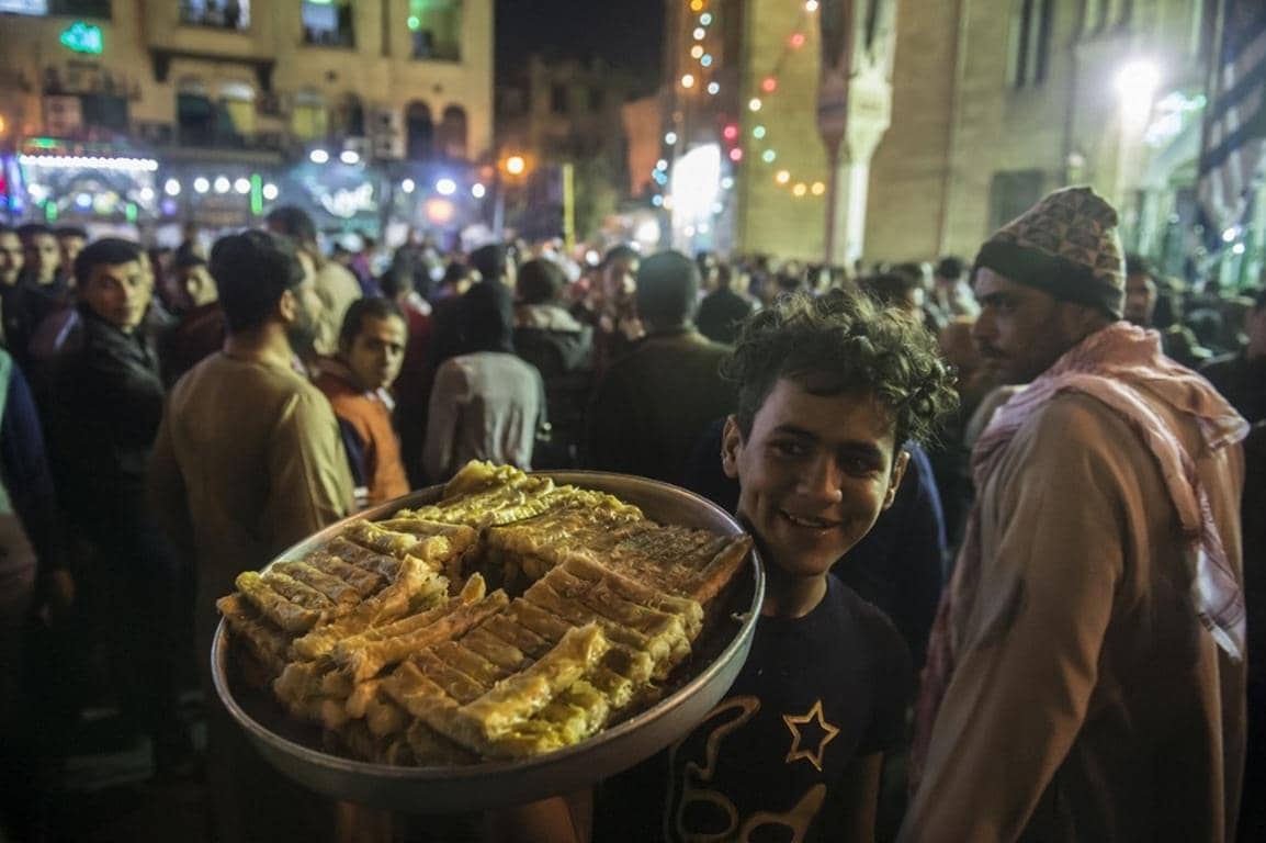 Young man smiling holding a large tray of sweets and bread, embodying the Prophet's Birthday Celebration 2025 charity efforts with donations like Bitcoin supporting the Muslim Ummah.