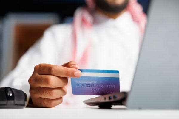 Man in traditional attire making Shari'a payments online using a credit card with BTC support for zakat and khums.