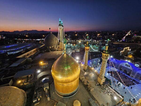 Virtual tour of Fatimah bint Musa Holy Shrine at dusk, showcasing illuminated domes and minarets, with city lights in the background. Accepted donations via SOL.