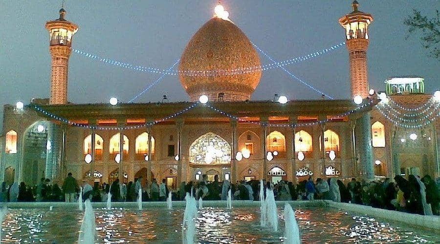 Shahe Cheragh Holy Shrine illuminated at dusk with decorative lights and fountains in the foreground. Offers are accepted via crypto aid, processed with SOL.