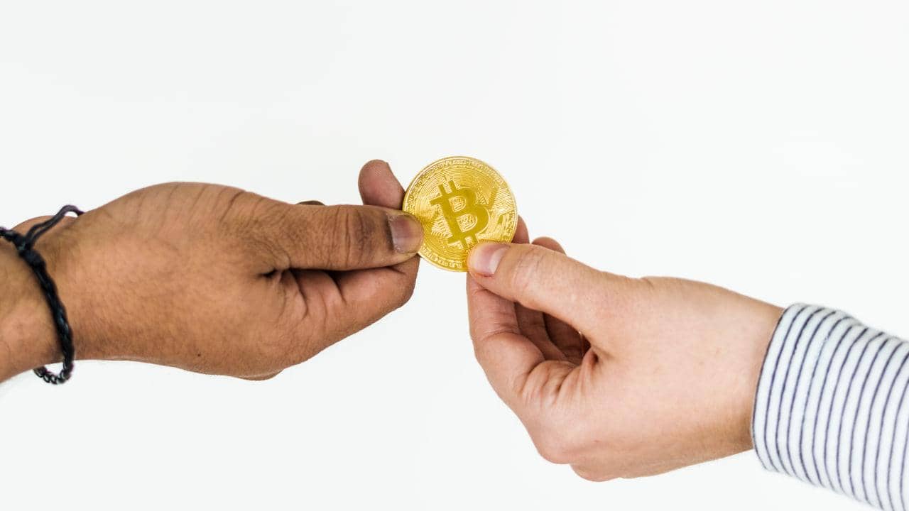 Bitcoin is exchanged between two hands, symbolizing the fulfillment of vows through crypto donations and charitable giving in Islam.