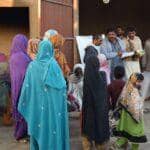 A diverse group of people, some wearing headscarves, stand in what appears to be a relief distribution area. Some men are gathered, possibly for aid distribution, with one holding a book. A child in a colorful headscarf walks past. The scene implies assistance provided through crypto processing, perhaps with USDT.