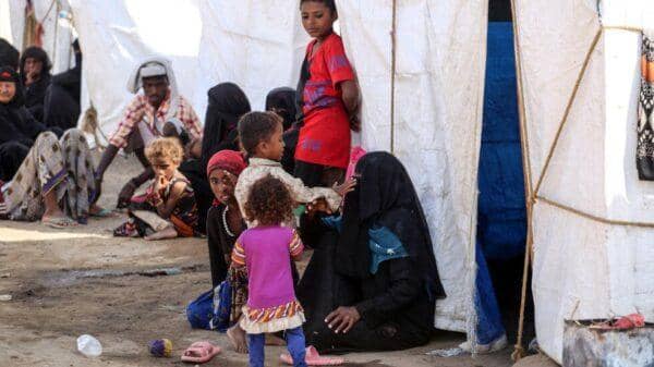 Children and adults in a displacement camp, some in traditional attire, receiving humanitarian aid. Supported by decentralized crypto donations of USDC.