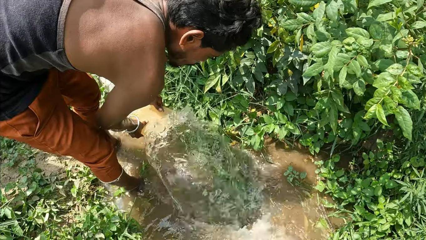 Man pouring water from a bucket into a small irrigation ditch to water plants, symbolizing providing food security support through crypto donations with BTC.