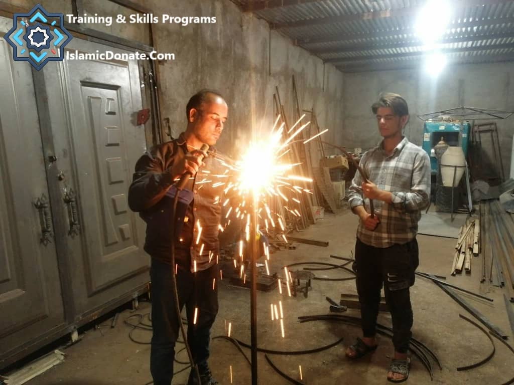 Two men participate in a welding training program, demonstrating skills development for sustainable livelihoods funded by cryptocurrency donations like Bitcoin.