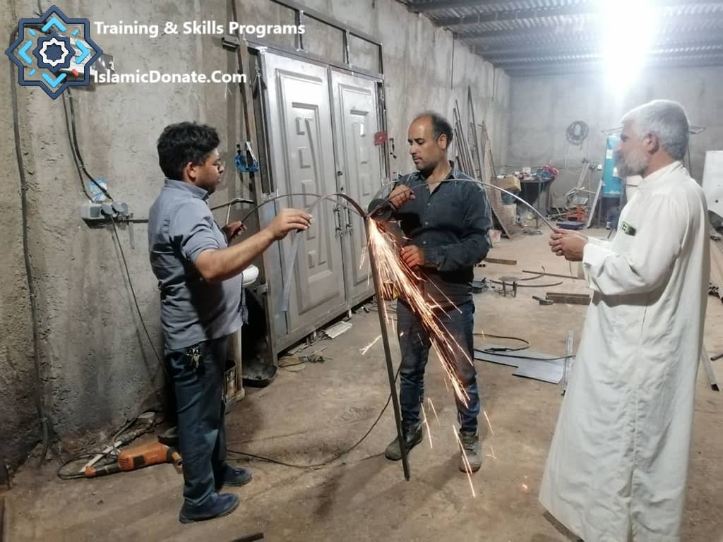 Three men in a workshop, two working on metal with sparks flying, illustrating training and skills programs funded by Sadaqah via cryptocurrency donations like RLUSD or PYUSD .