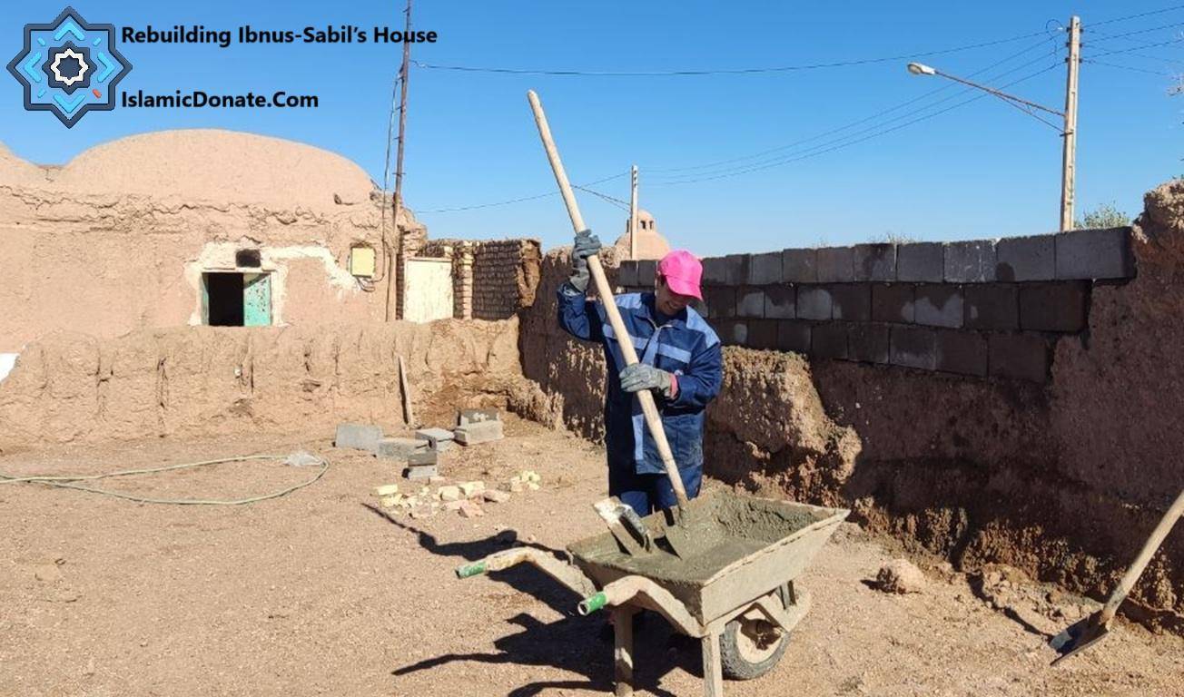 Construction worker mixing cement in a wheelbarrow for rebuilding a house, crypto zakat donation of ETH supports Islamic charity projects for the needy.