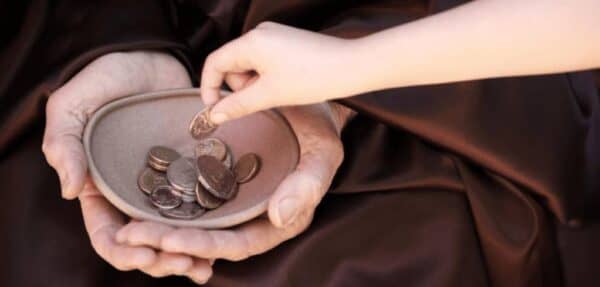 Close-up on an elder's cupped hands receiving coins from a child's hand, symbolizing daily Sadaqah and crypto donations for relief.