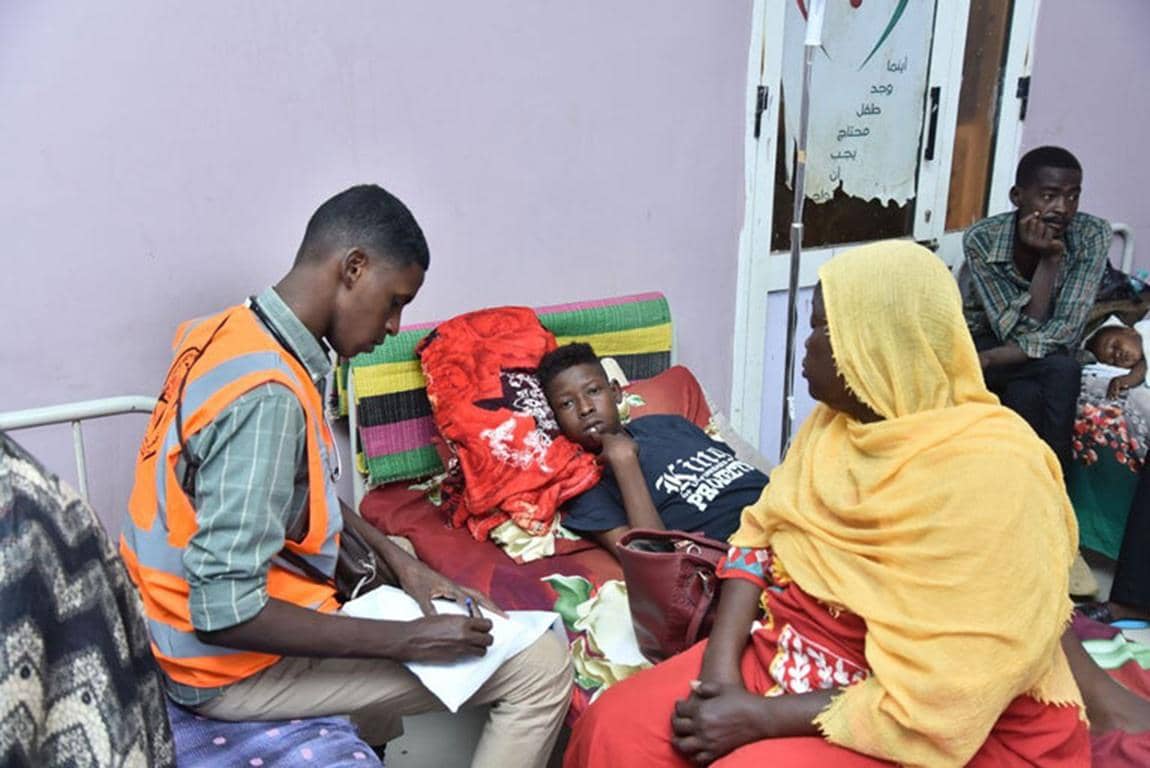 Healthcare worker noting patient details with woman and child during medical aid efforts, supported by ETH donations for general healthcare.