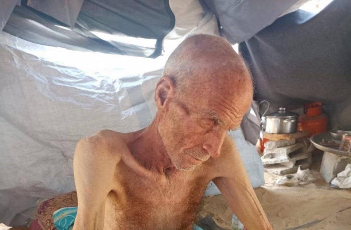 Elderly man in makeshift shelter, eyes downcast, thin frame. Supports skills training, toolkits, and food security with crypto donations like USDT to empower the poor.