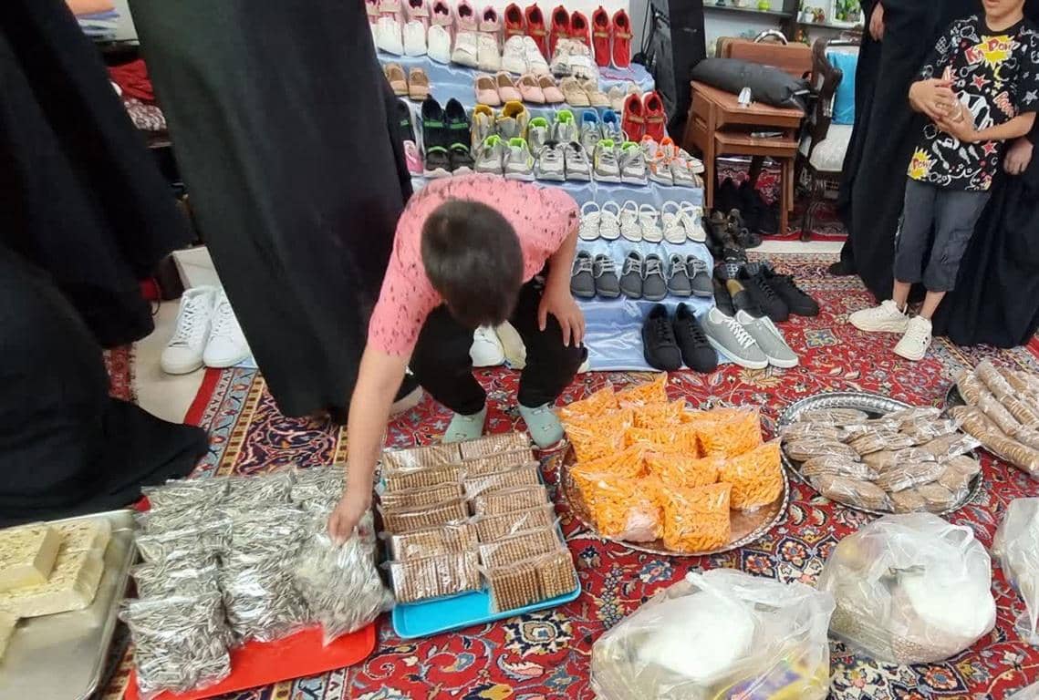 Boy selecting packaged goods next to stacks of shoes, with donations supported by LTC, fulfilling Khums obligations for orphans and needy.