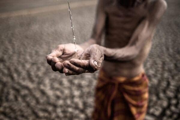 Hands cupped to receive water in a parched landscape, symbolizing urgent need and relief efforts, possibly supported by crypto donations via BTC.