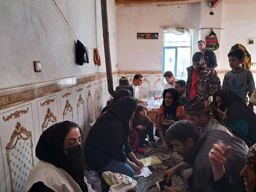 A group of people, including children, are gathered indoors, some sitting on the floor looking at papers. This scene depicts community support and is enabled by crypto donations like ETH.
