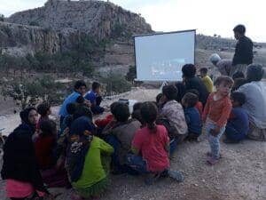 Children and adults gather outdoors to watch a projected movie in a rural village, symbolizing informal learning and community education efforts supported by crypto donations, like BTC.