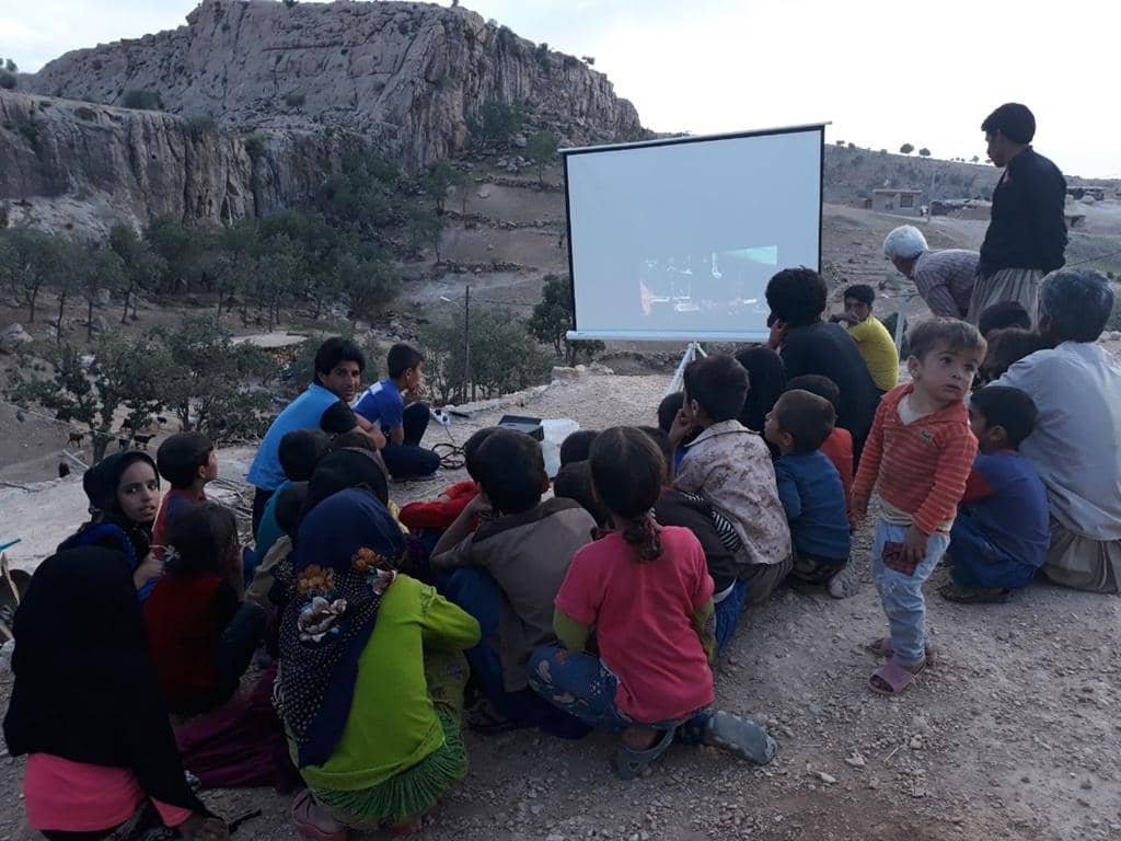 Children and adults gather outdoors to watch a projected movie in a rural village, symbolizing informal learning and community education efforts supported by crypto donations, like BTC.