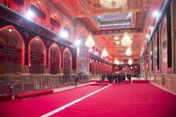 Interior of a grand hall with red carpets and ornate decorations, people walking on the carpet. Crypto donation for Nazr Mola and Kunde ki Niyaz via ETH.