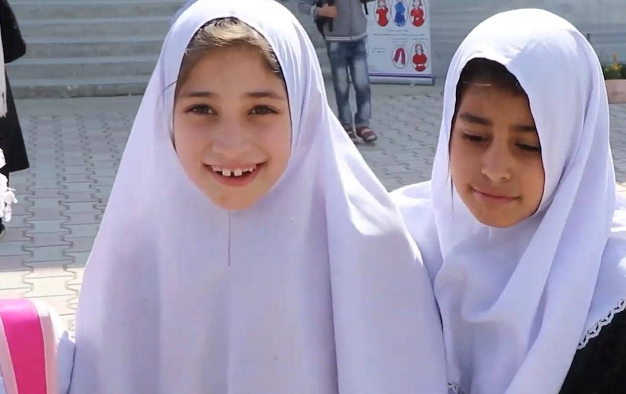 Two young girls in white hijabs smiling, representing the impact of IslamicDonate.Com's crypto Khums donations, possibly supporting education for orphans. Funds are processed via Arab Emirates Dirham.