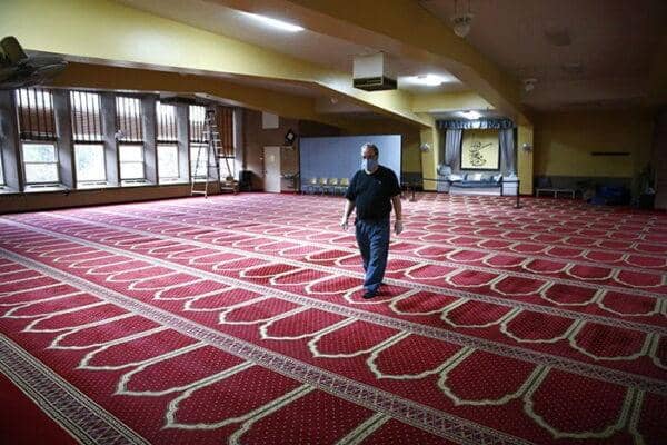 Man walking in a mosque prayer hall with prayer mats, highlighting community engagement and diverse perspectives with BTC processing.