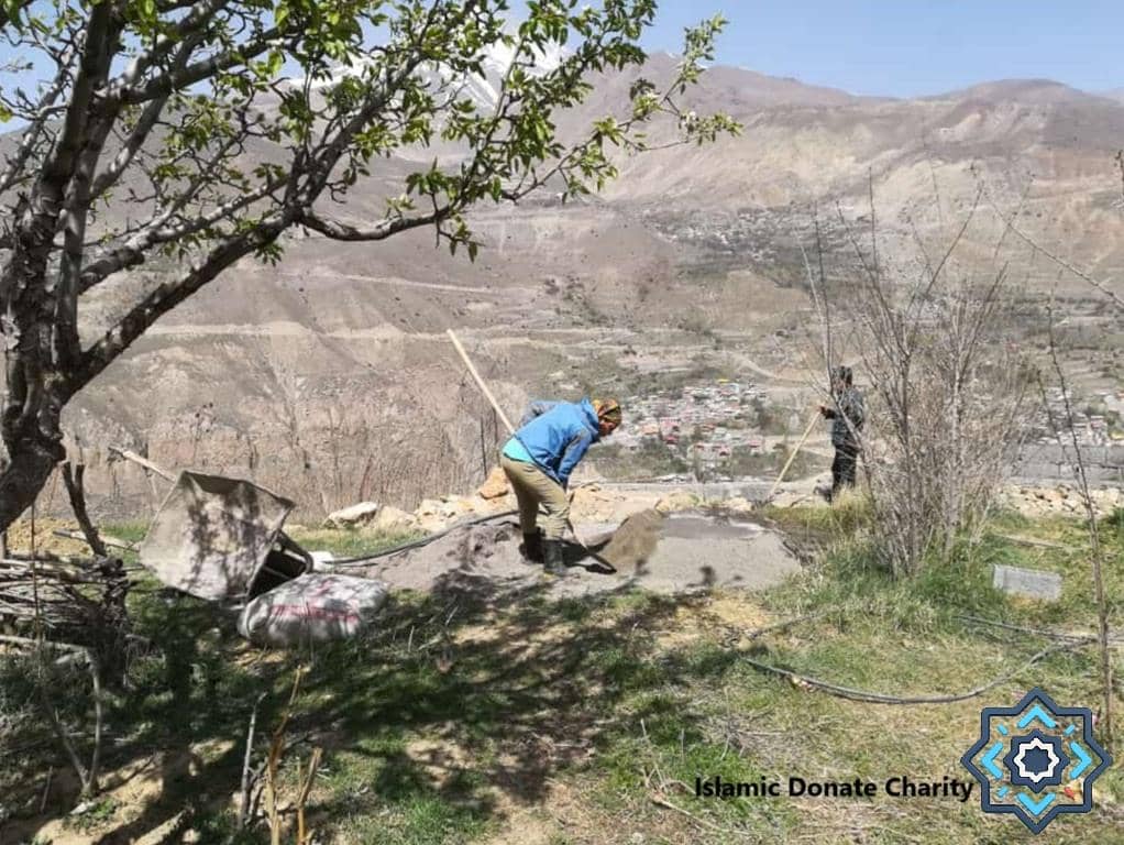 Two people working on a construction site in a hilly village, likely planting fig trees to combat desertification. Donations via SOL support sustainable agriculture and food security.