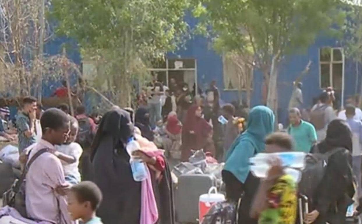 Crowd of displaced people with luggage, seeking humanitarian aid in Sudan and South Sudan, with crypto donations supporting relief efforts via Bitcoin.