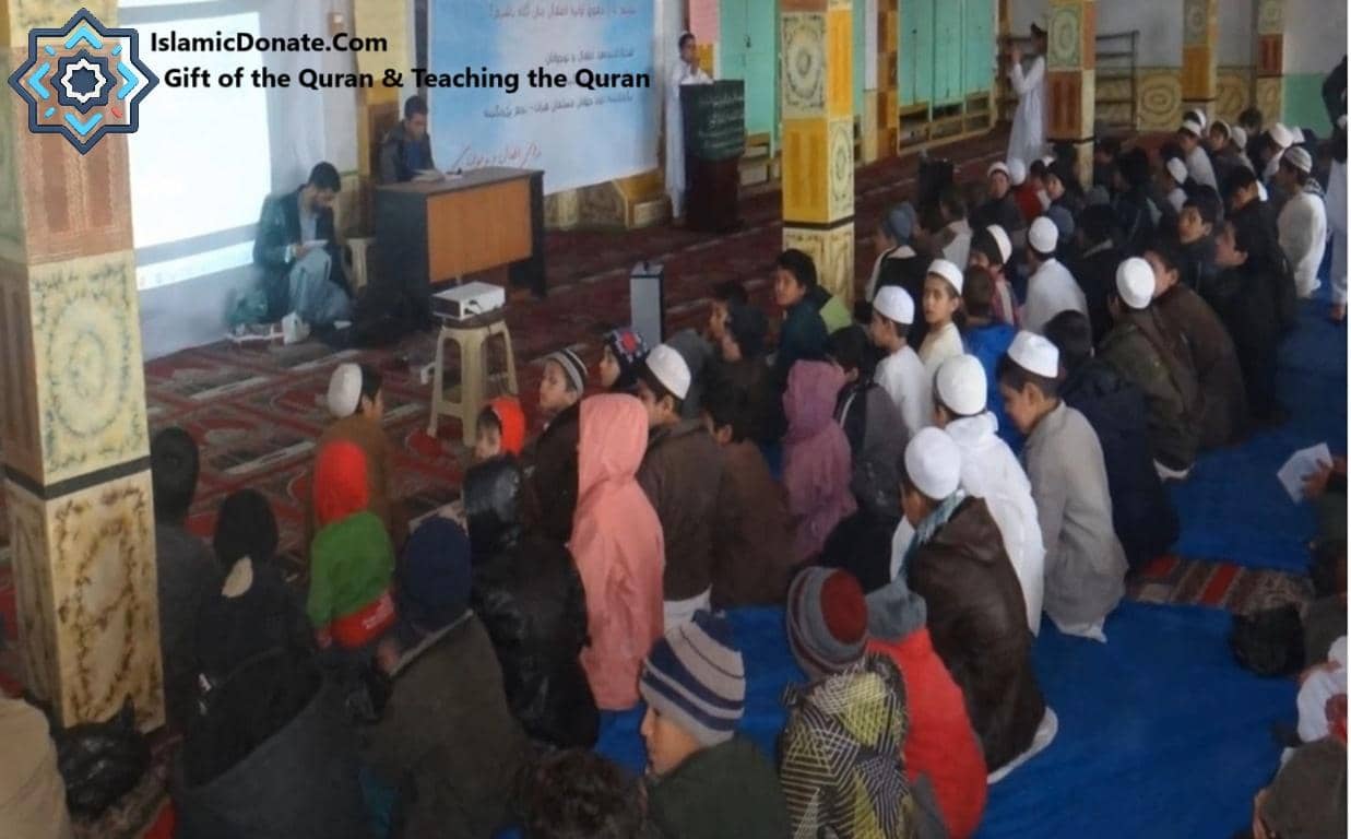 Children attending a Quranic education session, learning vital Islamic teachings, with one teacher presenting via a projector, supported by cryptocurrency donations like BTC.