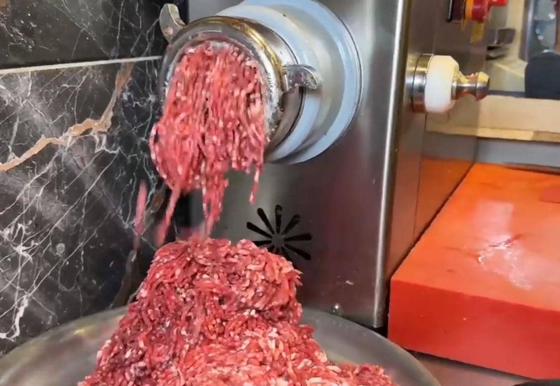 Ground meat exiting a meat grinder, ready for distribution. Supporting Qurbani and Aqeeqah donations with SOL cryptocurrency for Islamic charity.