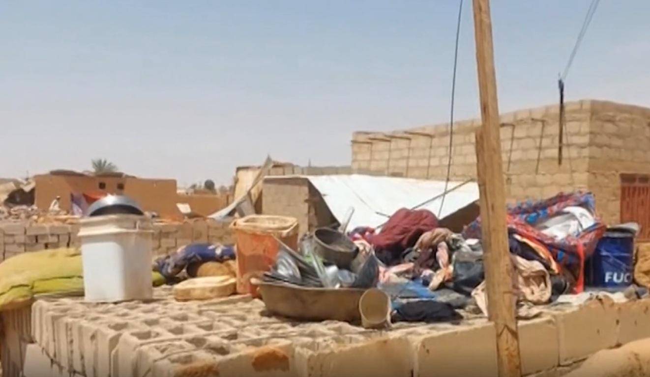 Damaged structures and scattered belongings in a crisis zone in Sudan or South Sudan, where cryptocurrency donations support humanitarian aid, including food and water. Your BTC donation brings relief.