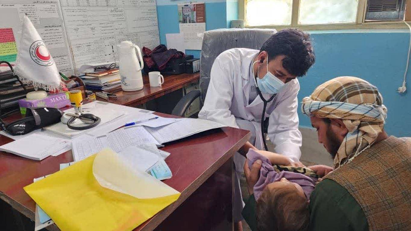 Doctor examines a child while their guardian looks on, with Red Crescent flag visible. Crypto donations support vital medical care, offering hope to vulnerable children via USDC.
